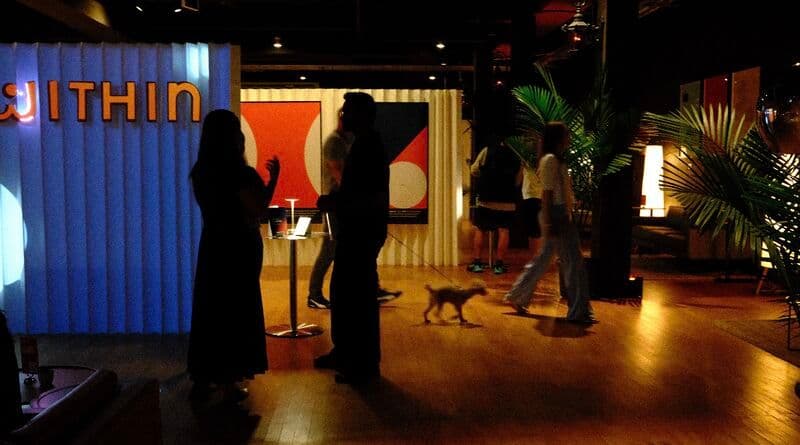 Visitors talking inside the Within Gallery on University Avenue in Palo Alto, lit exhibit panels behind them